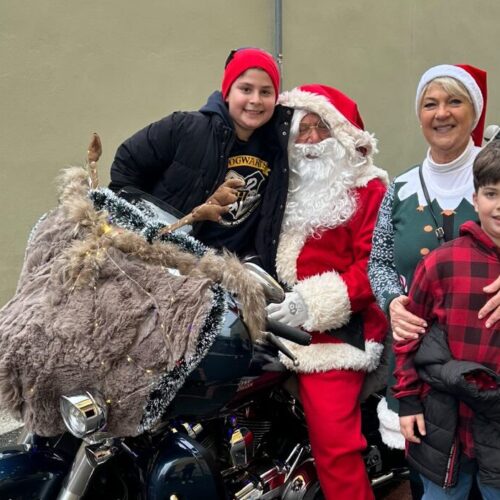 Un nonno Babbo Natale e una nonna elfa sulla Harley regalano sorrisi davanti alla Scuola De Amicis