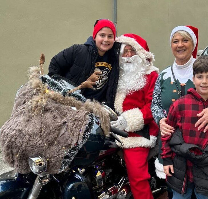 Un nonno Babbo Natale e una nonna elfa sulla Harley regalano sorrisi davanti alla Scuola De Amicis